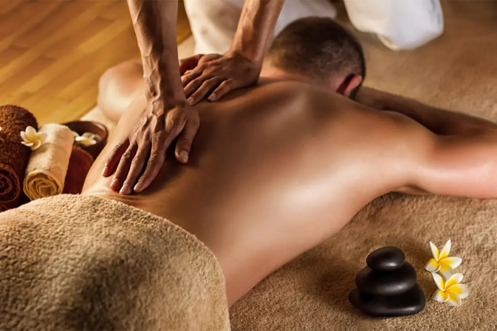 A gay male masseuse is giving a naked man a massage